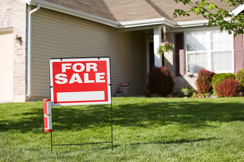 Red and white "For Sale" sign in front yard of suburban house.